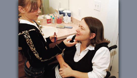 A picture of a woman sitting in a wheelchair with a little girl helping her with her makeup