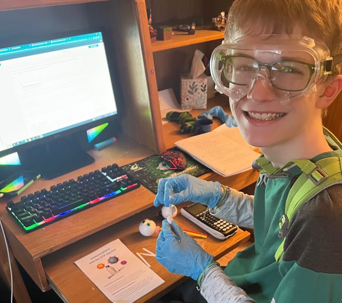 Boy with safety glasses and gloves in front of a computer working on a project.