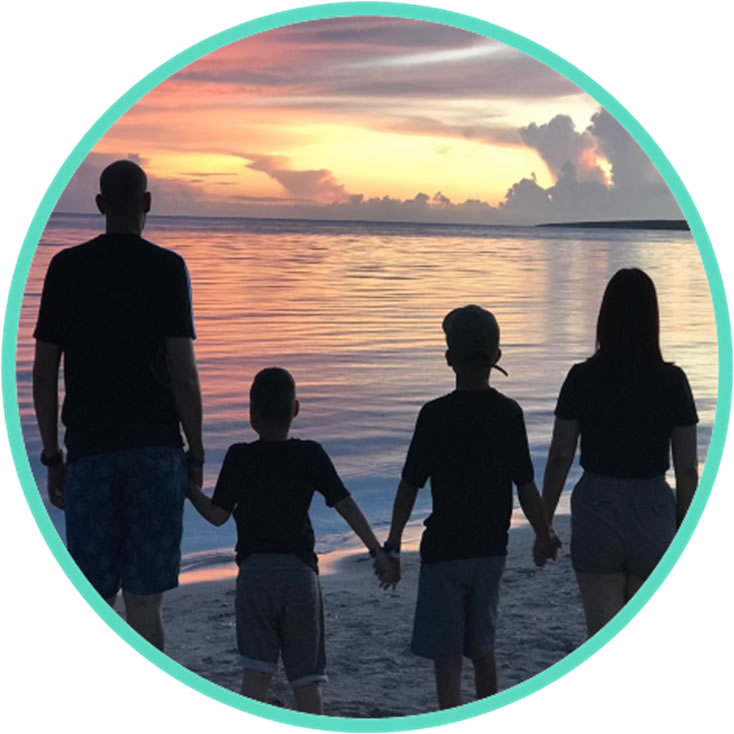 Image of three people up close with palm trees, grass and ocean in the background.