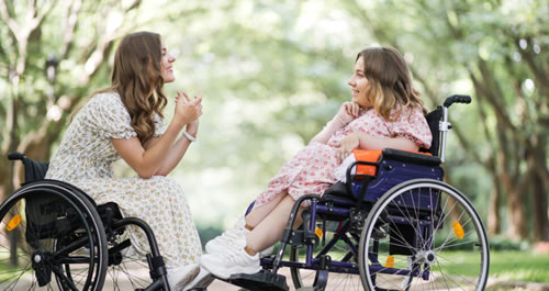 Two women in wheelchairs facing eachother in a park