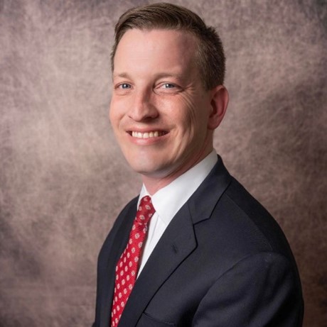 Image of a headshot of a man in a blue blazer, white buttoned downed shirt and red tie.