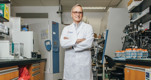 Scientist in a lab coat standing and crossing his arms.