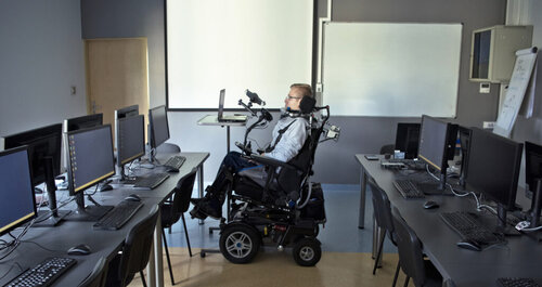 Man in wheelchair at desk in front of a laptop in a computer room