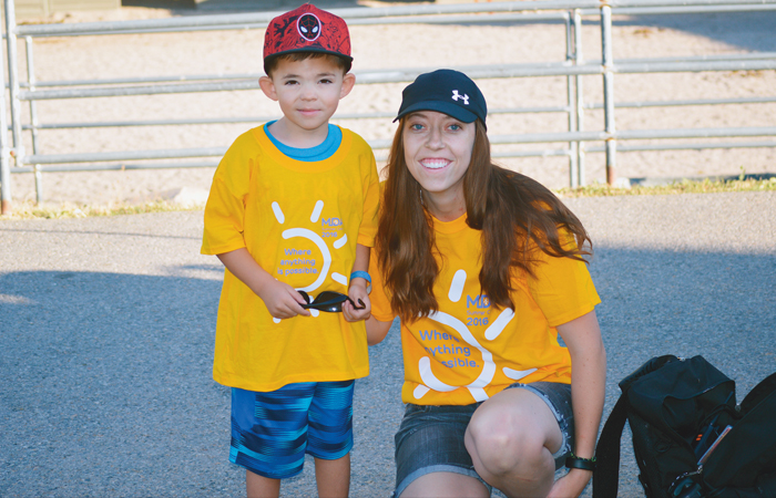 Whitney Jorgensen, a 25 year old MDA Shambassador, kneeling with a little boy at summer camp