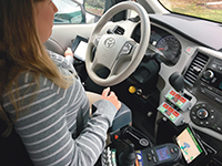 Casey Stark drives using a joystick hand control and dashboard computer monitor.