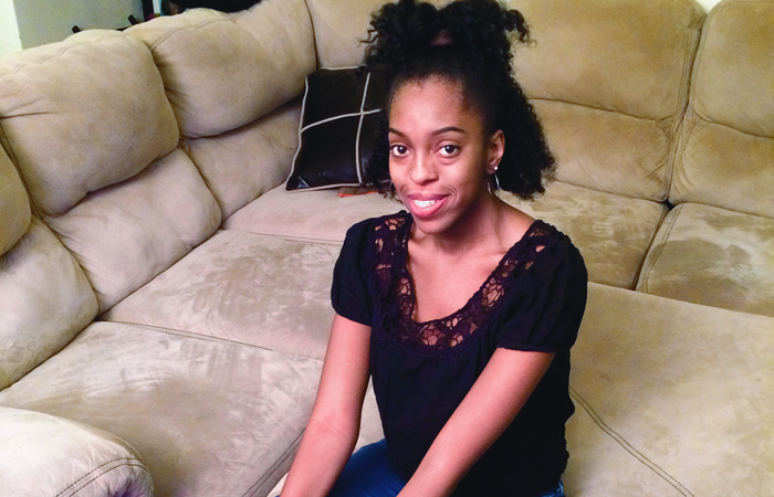 Brandi Hawkins, wearing a black blouse, sitting on a couch smiling