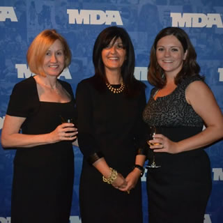 Three women standing in front of an MDA banner at WOWs 2012.