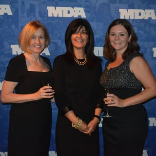 Three women standing in front of an MDA banner at WOWs 2012.
