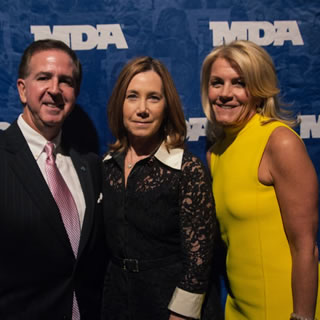 Three well dressed individuals in front of an MDA banner at WOWs 2014.