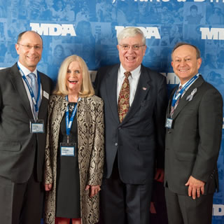 Four well dressed individuals in front of an MDA banner at WOWs 2015.