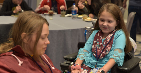 A photo of a little girl in a wheelchair at a conference.