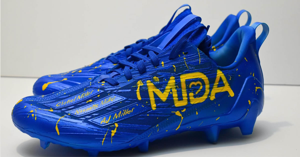 Bright dark blue footbal cleats with the MDA logo on them, splattered with yellow.