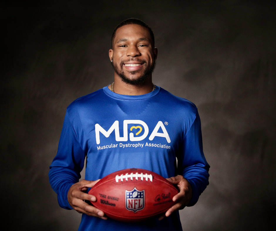 Image of a football player in a long sleeve blue MDA shirt holding a football.