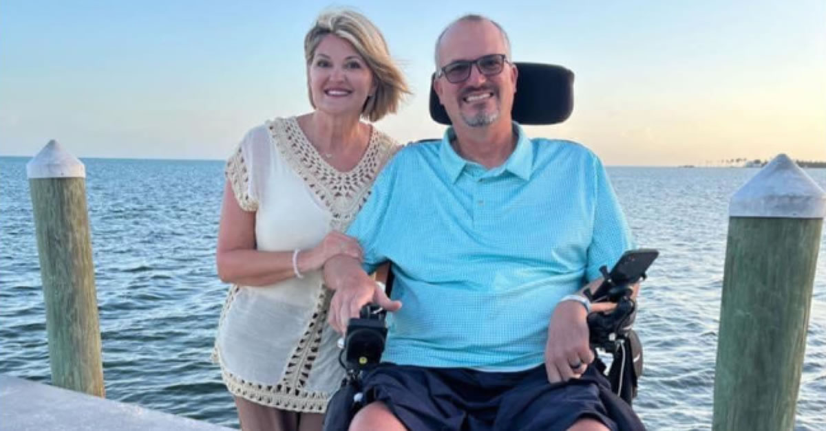 A Woman standing next to a man in a wheelchair on a pier.