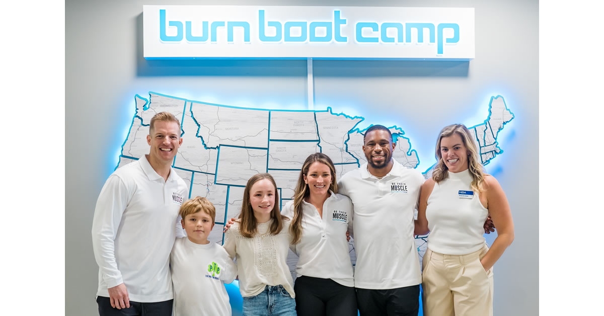 Men, Women, and children standing with arms interlocking in front of a big United States Map, with the Burn Boot Camp logo sign above them.