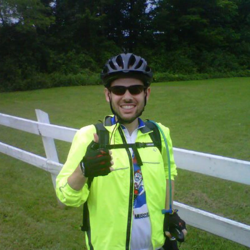 A man in a mountain bike helmet standing, and giving a thumbs up