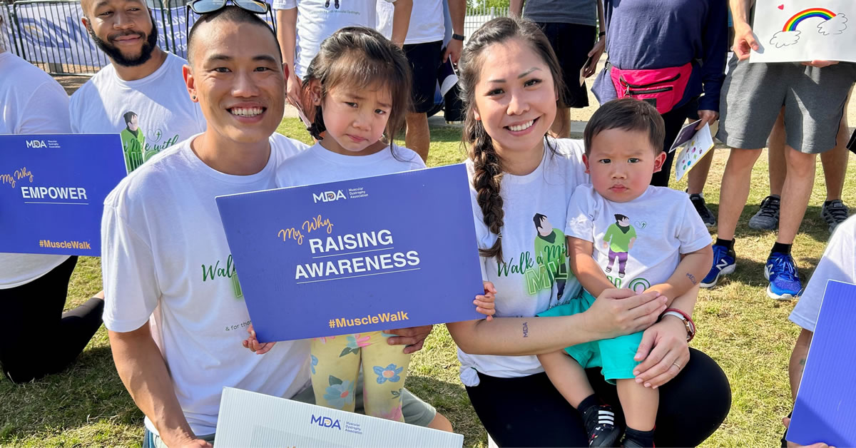 A family kneeling on the grass holding Muscle Walk Posters.