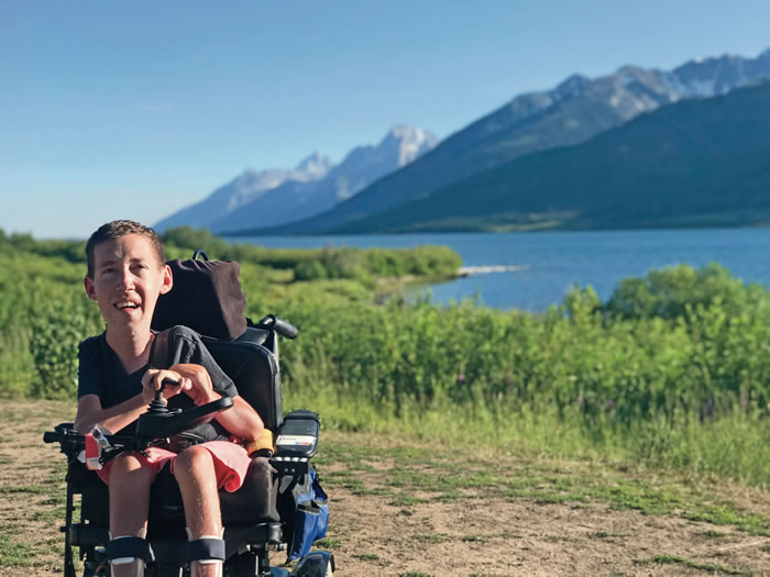 A picture of Shane Burcaw at the side of a lake, with mountains in the background