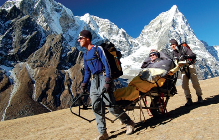 A picture of three people climbing a mountain, one of them in a specially made mountain climbing wheel chair